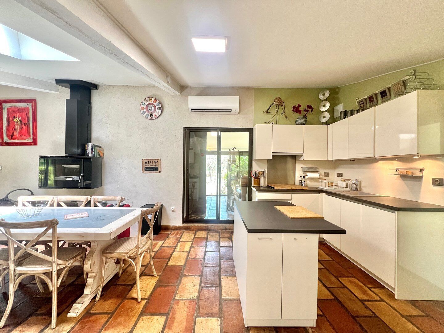 Una cocina con gabinetes blancos, una estufa negra y un comedor con sillas de mimbre.
