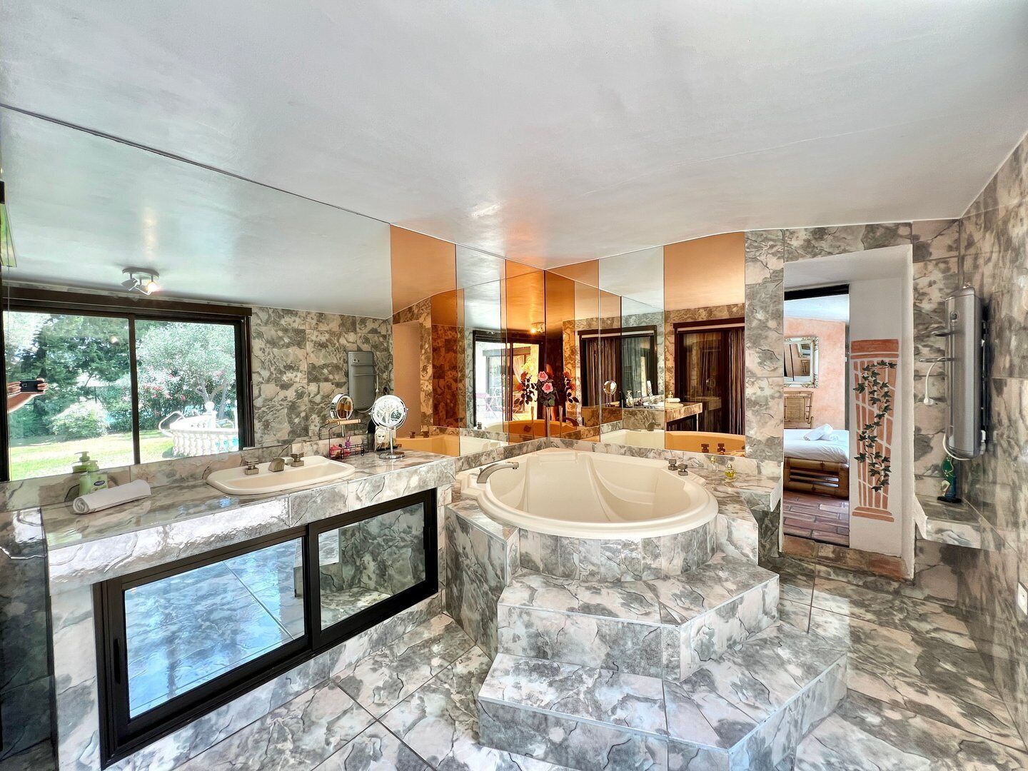 Une salle de bain luxueuse dotée d’une grande baignoire, d’un meuble-lavabo avec un miroir et d’une fenêtre offrant une vue sur l’extérieur.