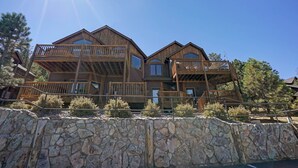 A multi-story wooden building with balconies and large windows, surrounded by stone walls and trees. - Mount Meeker 26B - Cozy Condo with Private Hot Tub - Mountain and Lake Views (Estes Park)