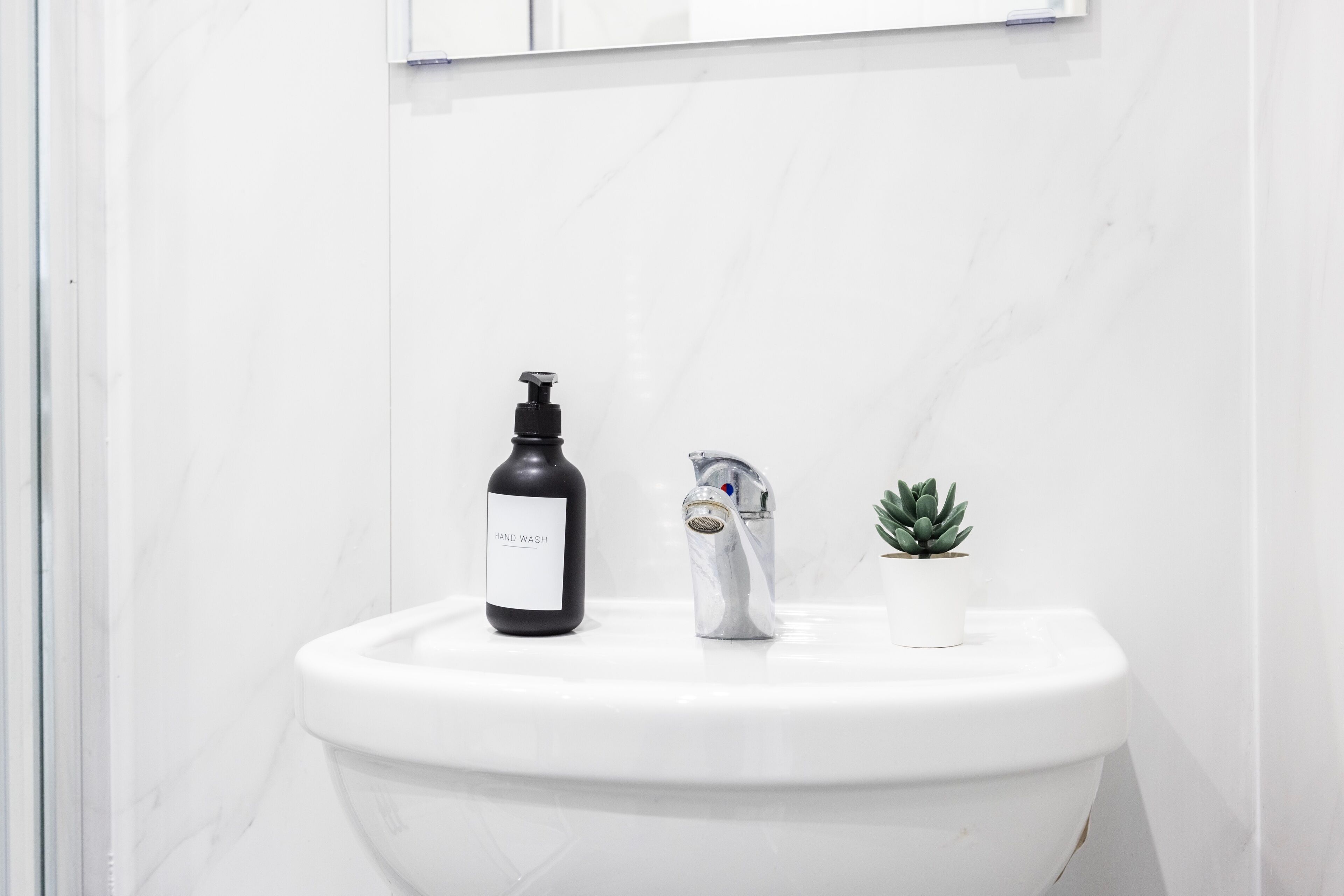 A bathroom with a white toilet, a black hand wash bottle, a silver faucet, and a small potted plant.
