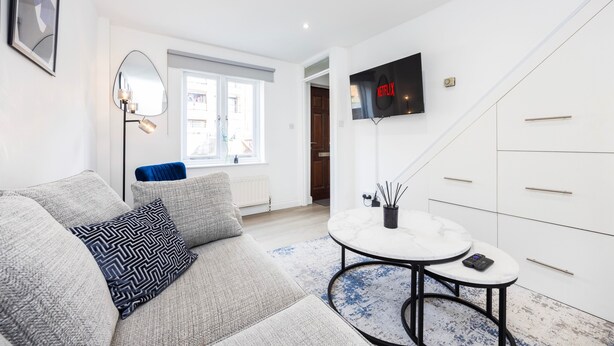 Un salon moderne avec un canapé, une table basse, un téléviseur fixé au mur et une vue sur l’extérieur par une fenêtre.