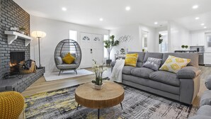 Una sala de estar moderna con chimenea, un sofá gris, cojines amarillos y una mesa de centro redonda.
