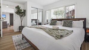 Un dormitorio moderno con una cama grande, un plaid verde y vistas al exterior a través de amplios ventanales.