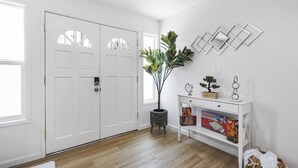 Una habitación con una puerta blanca, una planta en maceta, una consola blanca y cajas de Monopoly, además de un adorno en la pared.