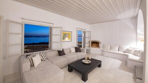 A modern living room with a large window, a fireplace, and a sofa set. - Charming 5-bed Villa in Mykonos (Mykonos)