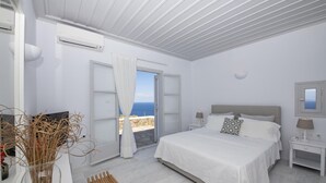 A bedroom with a large bed, a nightstand, a bedside table, a mirror, and a view of the sea. - Charming 5-bed Villa in Mykonos (Mykonos)