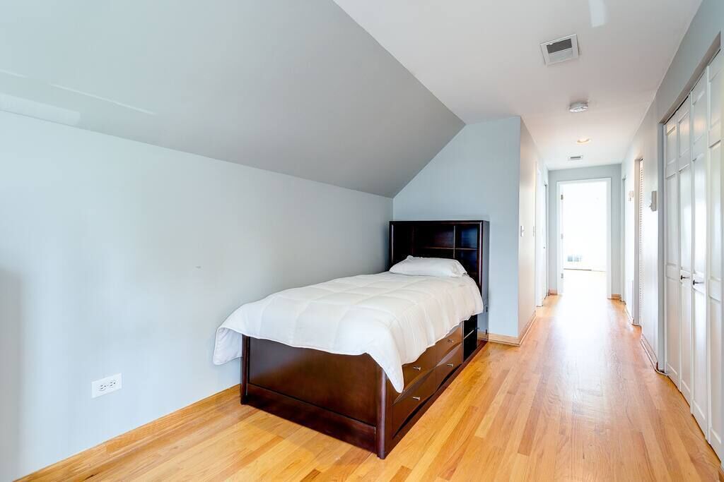 A bedroom with a bed, wooden flooring, and a hallway leading to a door.