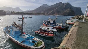 Un puerto con barcos amarrados, agua tranquila y montañas al fondo.
