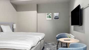 Une chambre d’hôtel avec un lit, une petite table ronde et une chaise, ainsi que deux tableaux encadrés accrochés au mur.