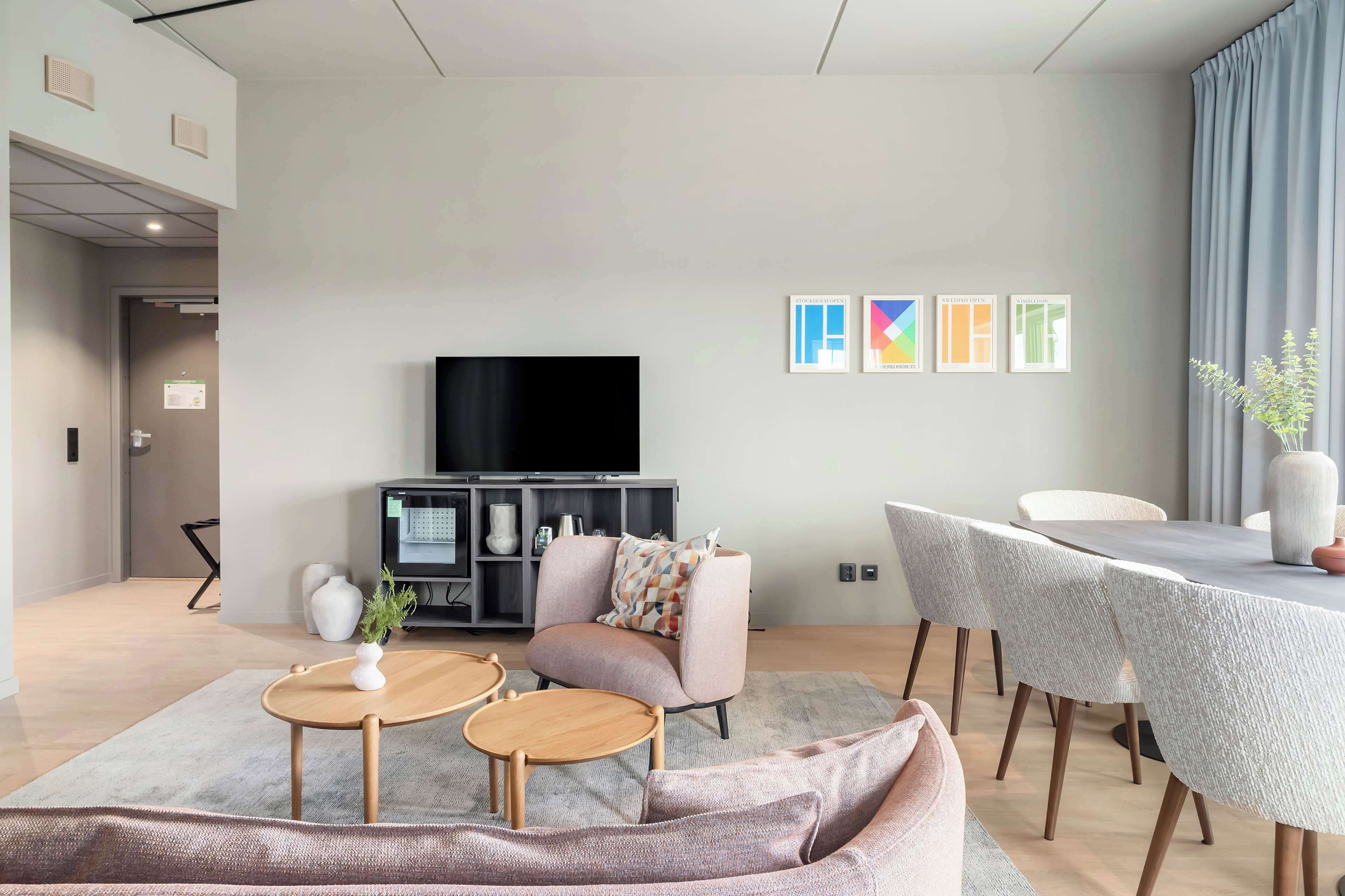A modern living room with a sofa, two small tables, a TV, and a dining table with chairs.