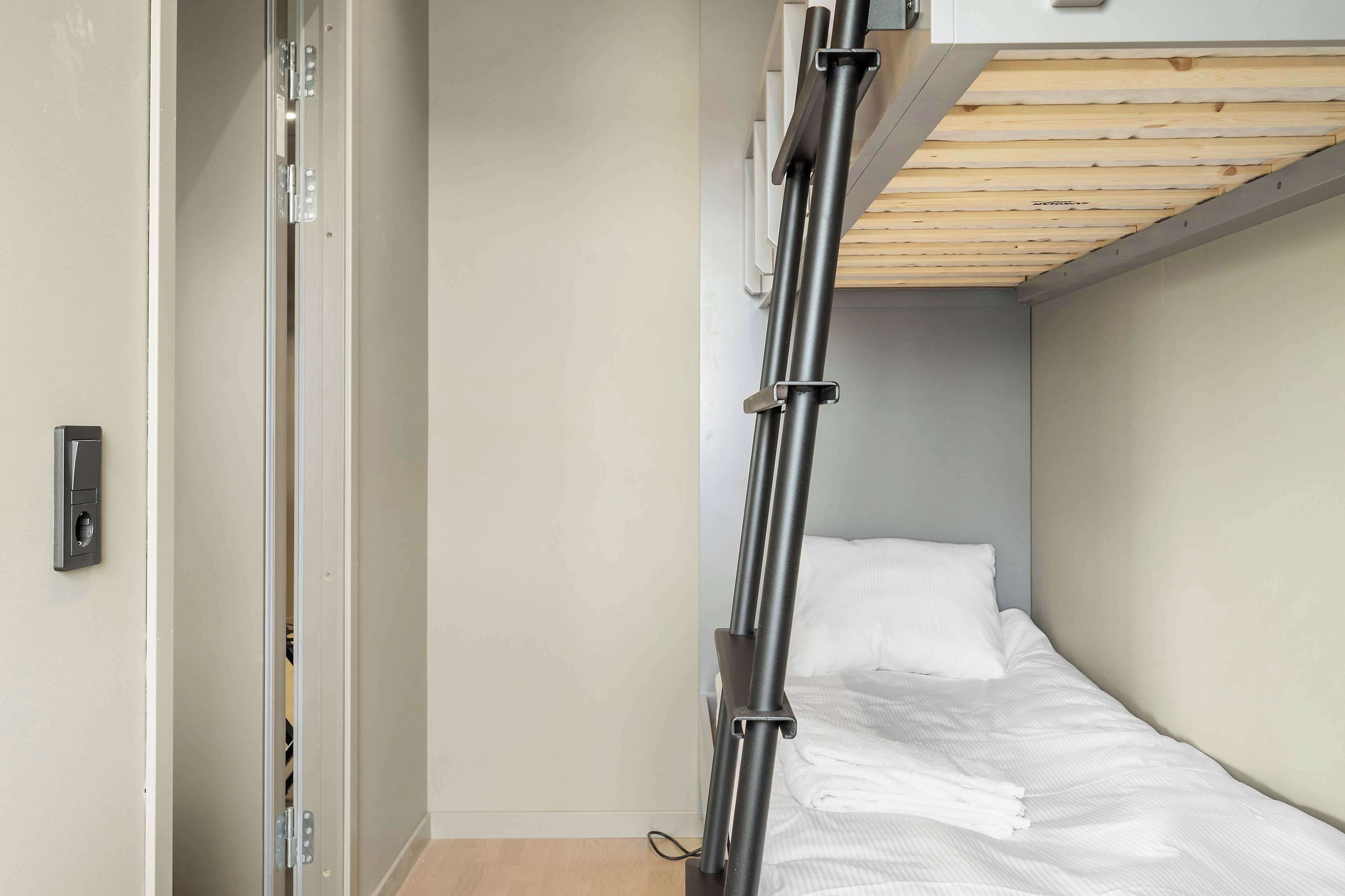 A compact room with a bunk bed, a sliding door, and a wooden ceiling.