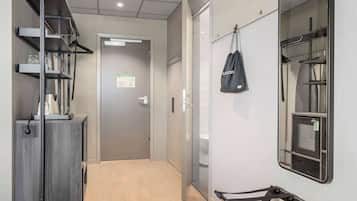 A hallway with a grey wardrobe, a black bag hanging on the wall, and a mirror reflecting a window.