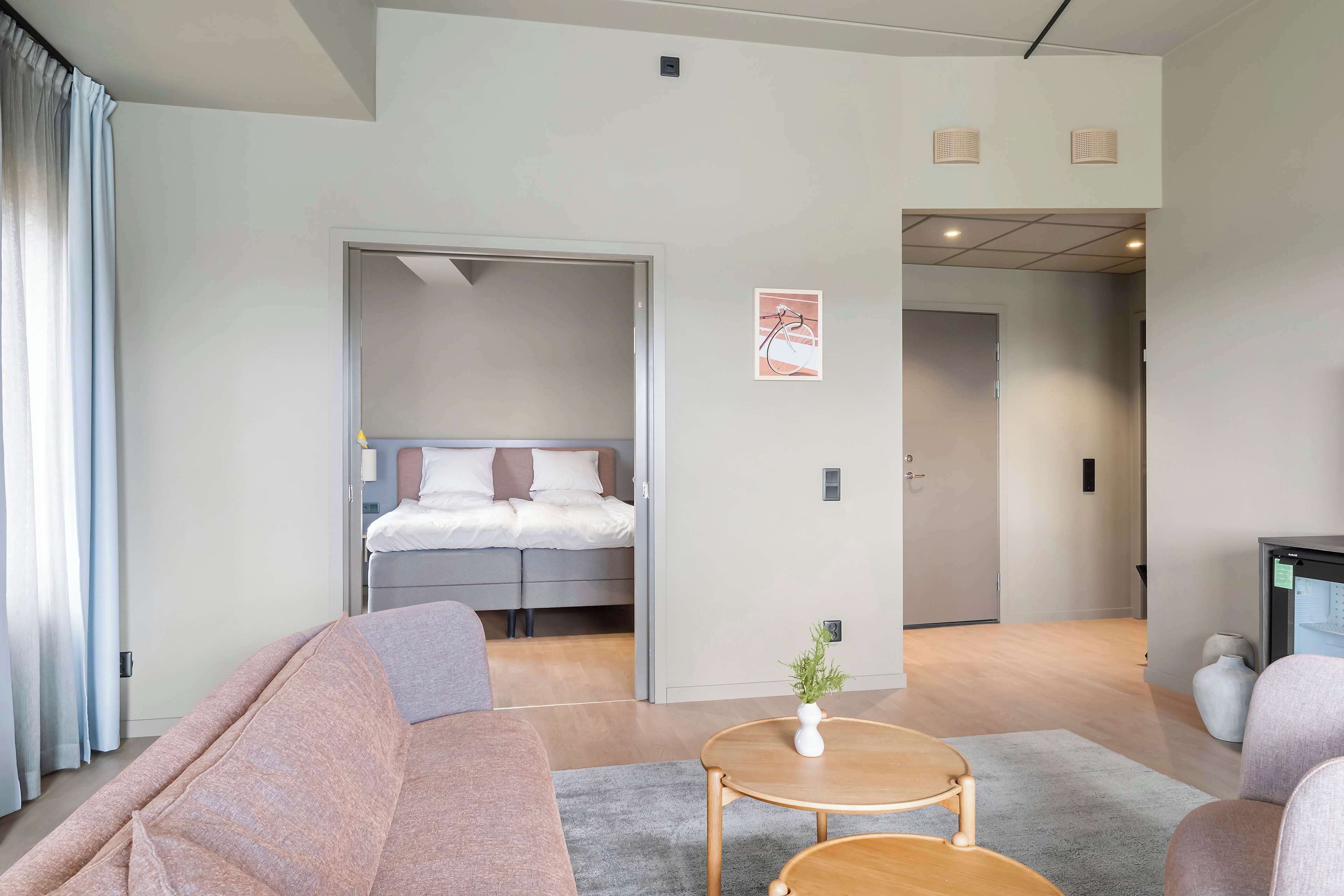 Una habitación de hotel moderna con una cama, un sofá, una mesita y una planta en maceta.
