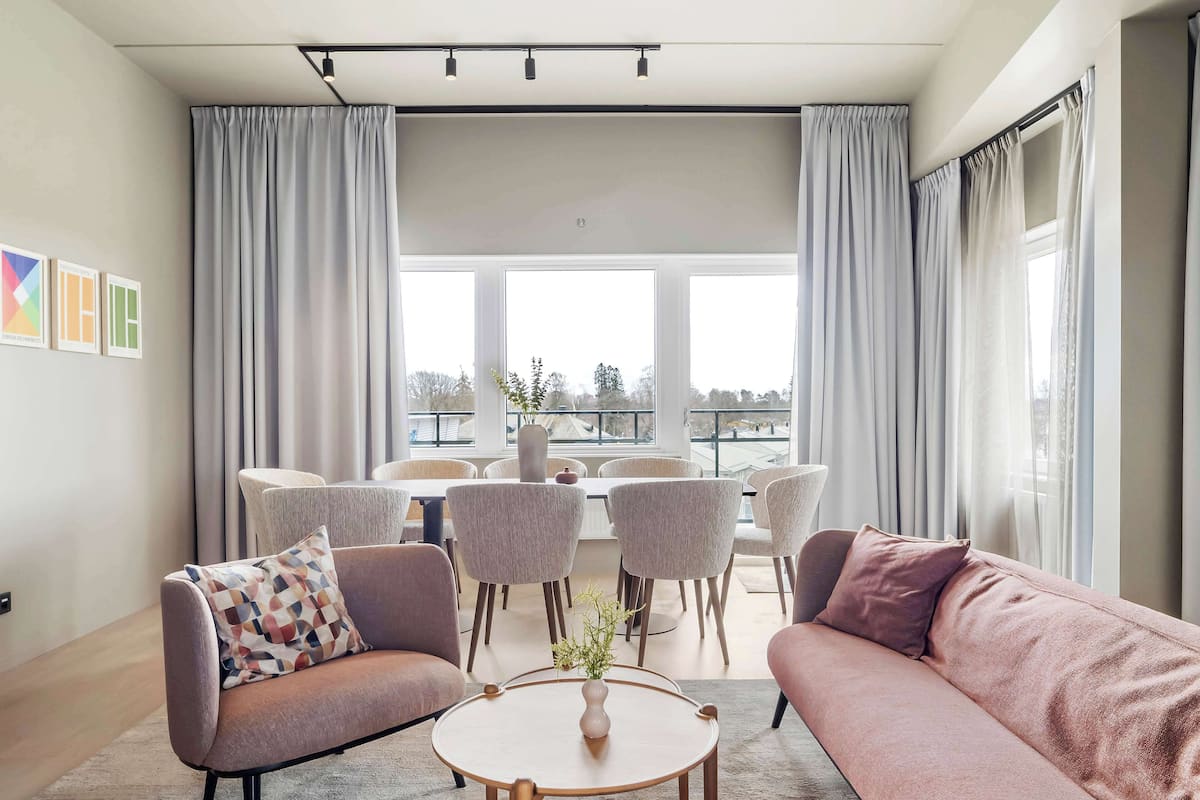 A modern living room with a sofa, armchair, and round coffee table. There is a dining table with chairs in the background.