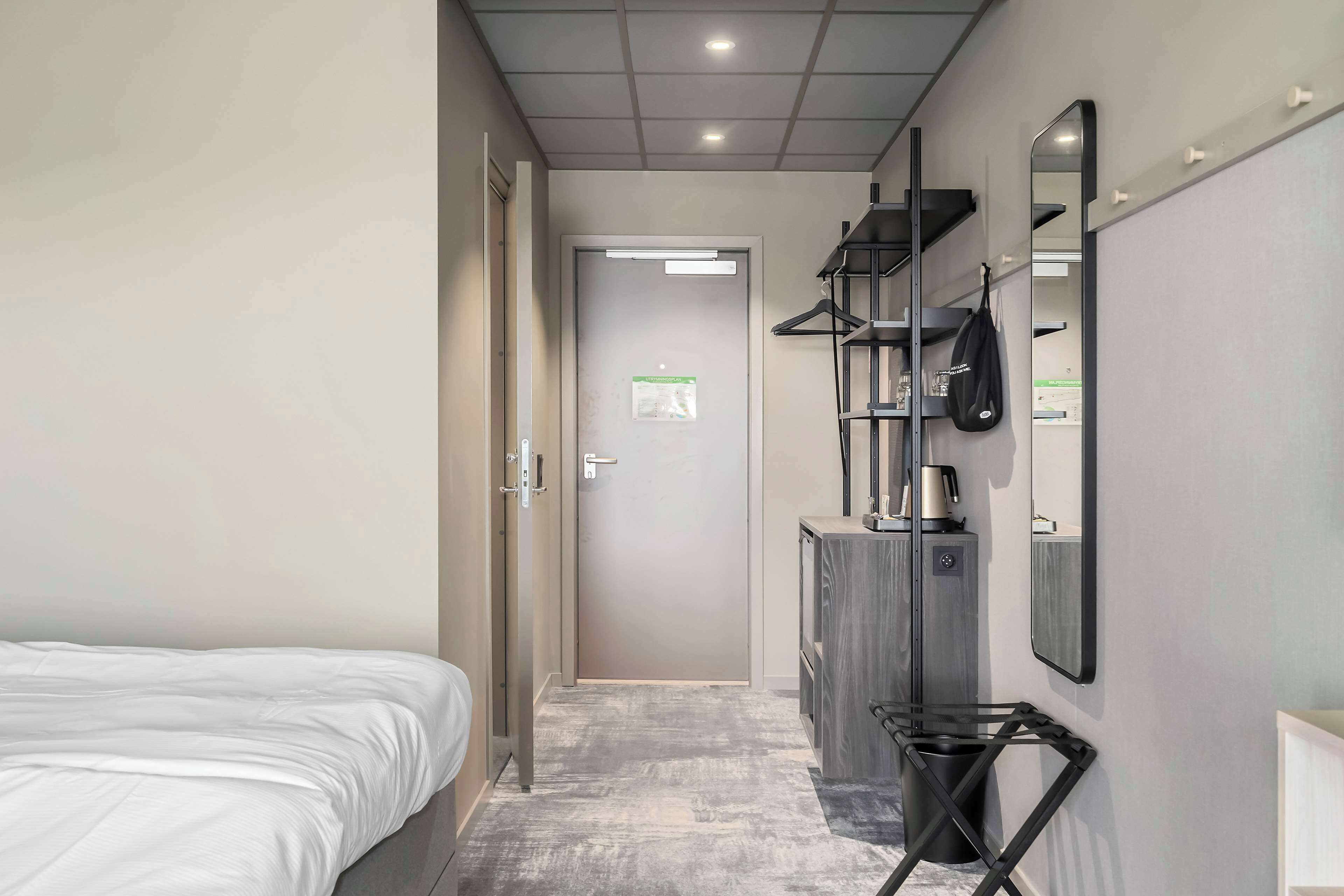 Een hotelkamer met een bed, een kledingkast, een spiegel en een prullenbak.