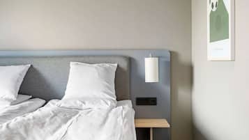 Una cama bien hecha con sábanas blancas, cabecera gris y mesita de noche con lámpara.