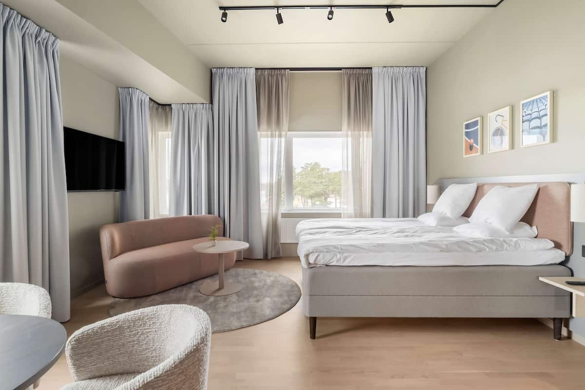 A modern bedroom with a bed, a sofa, a round table, and a TV.