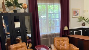 A living room with two leather armchairs, a wooden coffee table, a TV on a stand, a potted plant, and a window with curtains. - Sailor's Cove Studio. (St. Augustine)