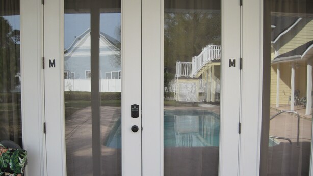 A set of white sliding doors with a keypad lock, leading to a backyard with a swimming pool and a covered patio area. - Sailor's Cove Studio. (St. Augustine)