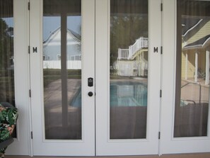 Weiße Schiebetüren mit Zahlenschloss, die zu einem Hinterhof mit Schwimmbecken und einer überdachten Terrasse führen.