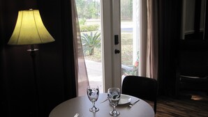 A hotel room with a round dining table set for two, a lamp, and a view of the outdoors. - Sailor's Cove Studio. (St. Augustine)