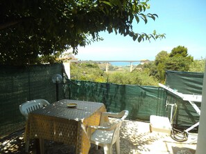 Un patio con una mesa y sillas, vista a un puente y una cerca verde.
