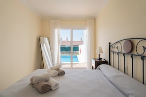 A hotel room with a bed, a view of a swimming pool, and a balcony.