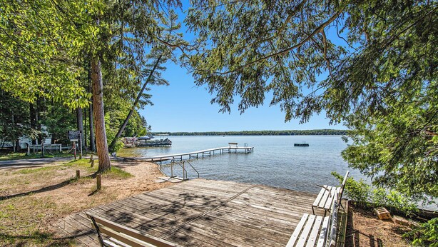 A wooden dock extending into a calm lake, surrounded by trees and benches. - Cozy Cottage w/ Shared Neighborhood Lake Access (Traverse City)