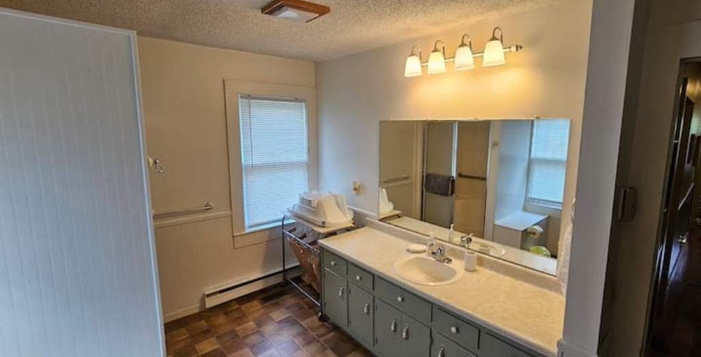 A bathroom with a double sink, a large mirror, and a window with blinds.