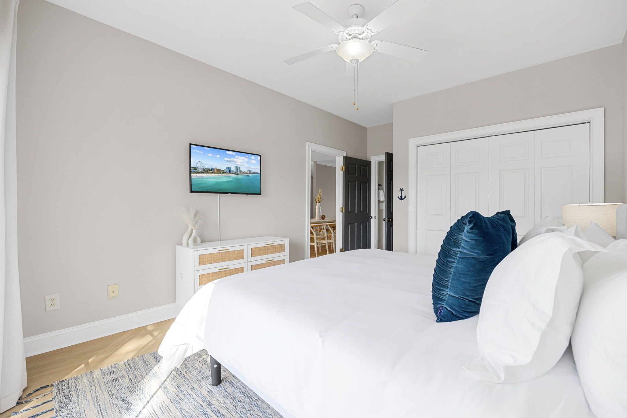 Une chambre à coucher comprenant un lit, un téléviseur, un ventilateur de plafond, une porte et un bureau avec une chaise.