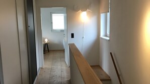 Ein schmaler Gang mit Holzboden, einer Holzhandläufe und einem Fenster am Ende.