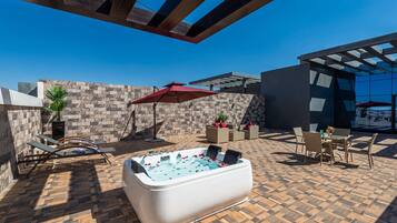 A rooftop patio with a hot tub, lounge chairs, and outdoor furniture.