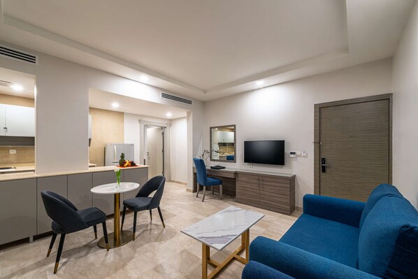 A modern living room with a blue sofa, a small round table, and a TV mounted on the wall.