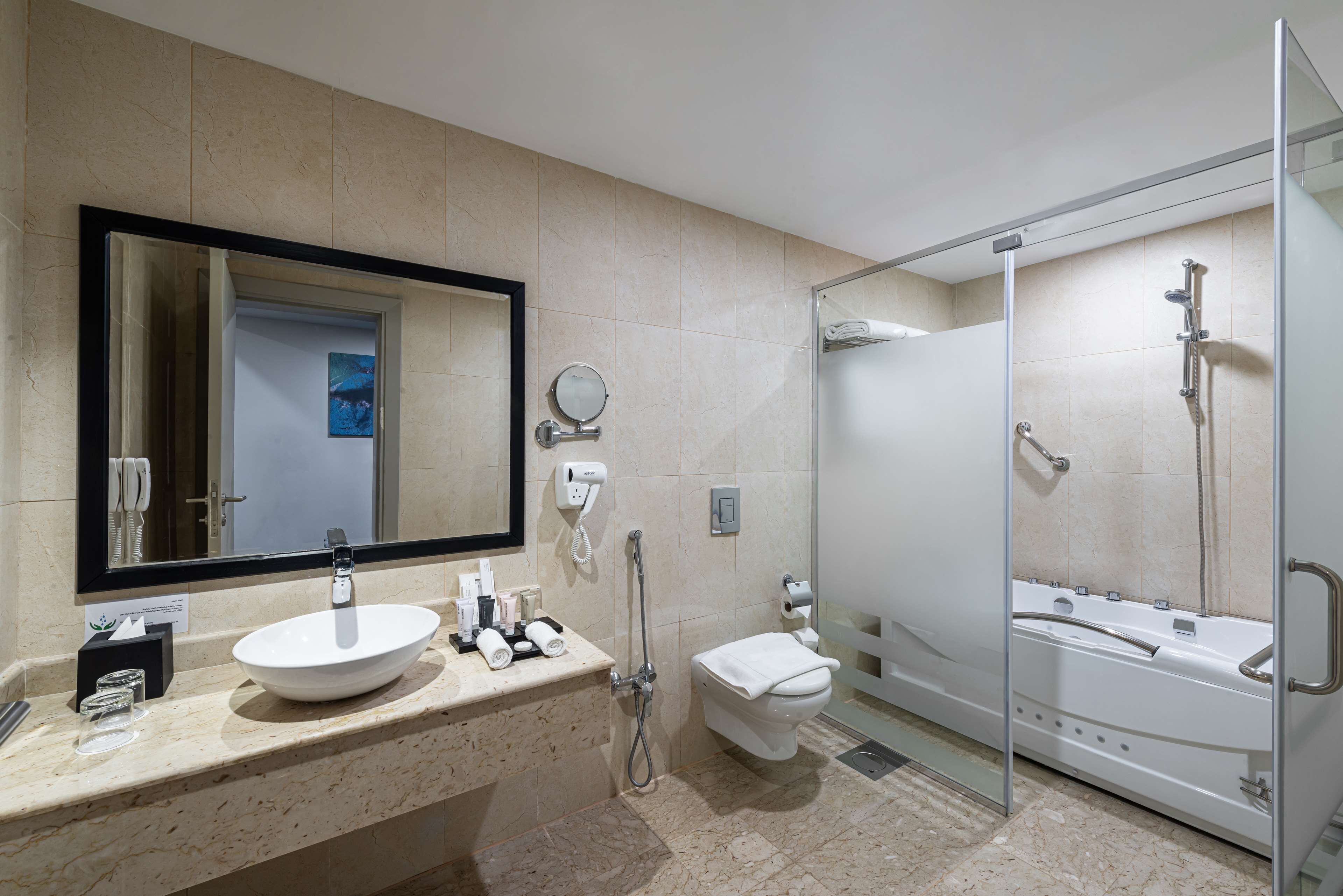 A modern bathroom with a large mirror, a sink, a toilet, and a glass-enclosed shower area.