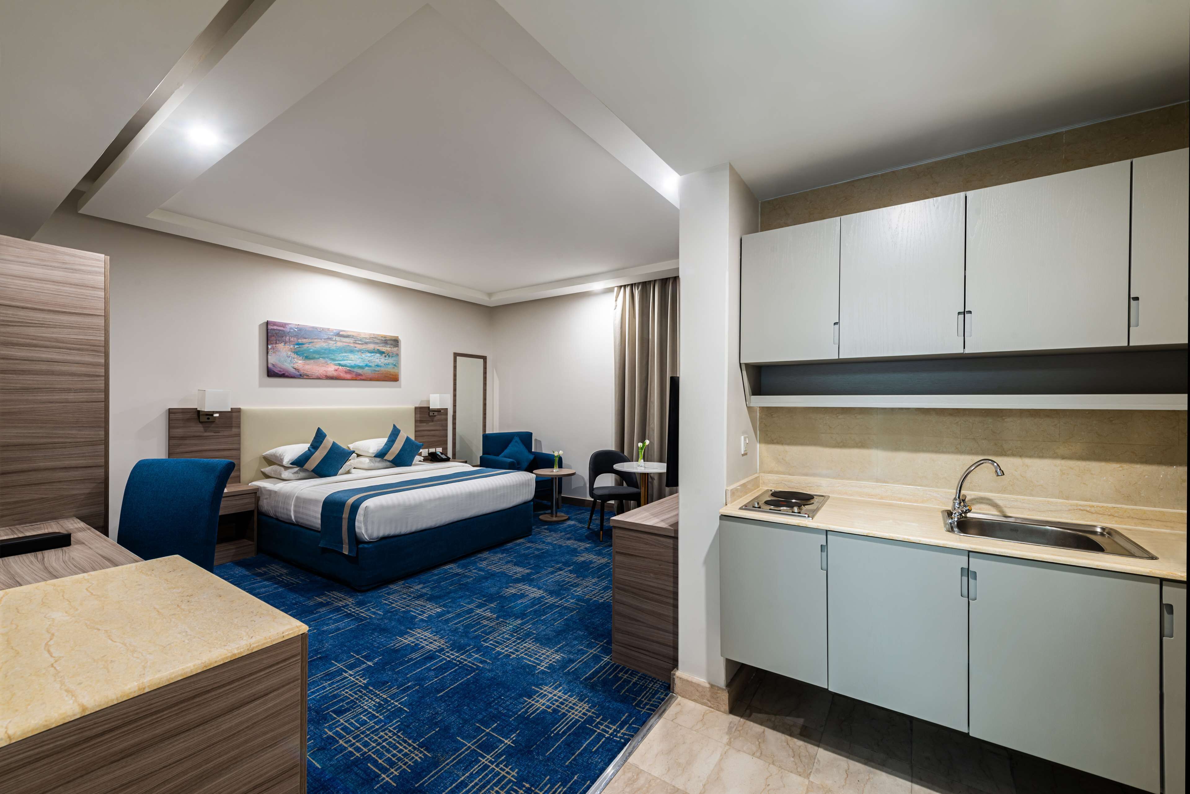 A hotel room with a bed, desk, chair, and kitchenette.