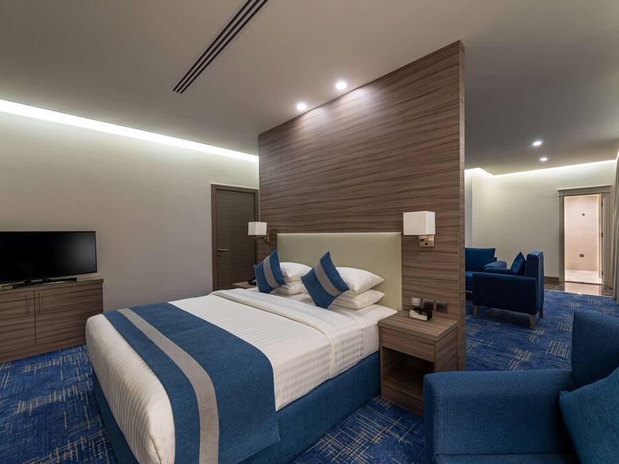 A hotel room with a large bed, a TV, a desk, and a seating area.