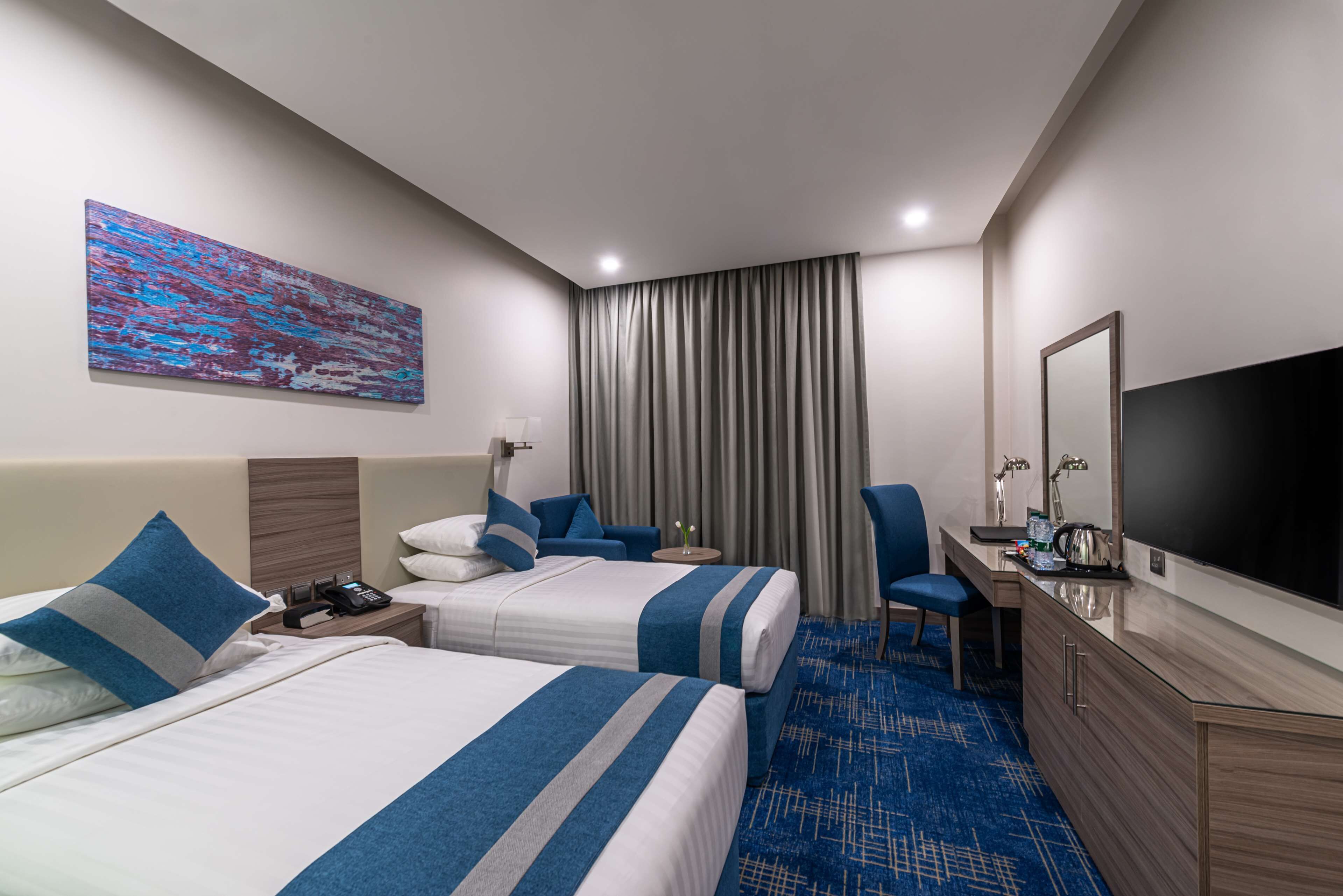 Habitación de hotel con dos camas, un escritorio, una silla, un televisor y un cuadro en la pared.