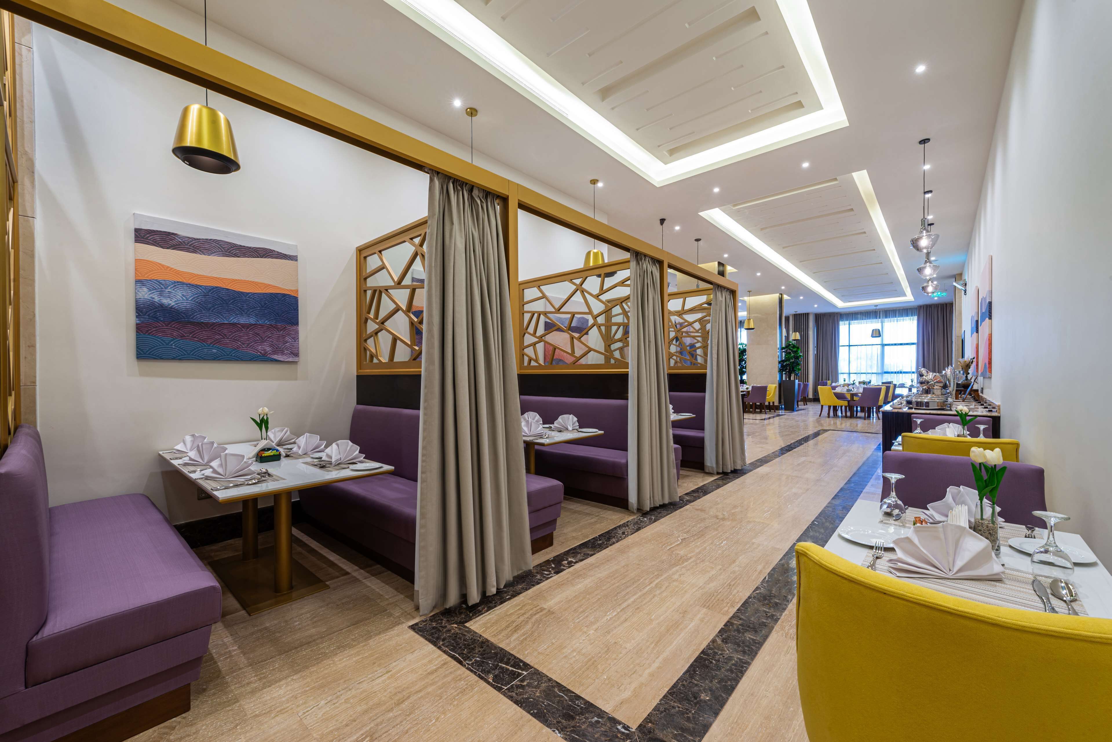 A modern restaurant with purple booths and yellow chairs, featuring a geometric wall design and a ceiling with recessed lighting.