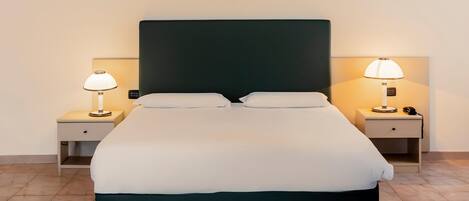 A neatly made bed with a dark headboard, two bedside tables with lamps, and a tiled floor.