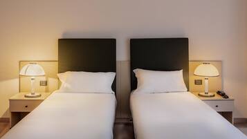 Una camera d'albergo con due letti singoli, ognuno con un comodino e una lampada.