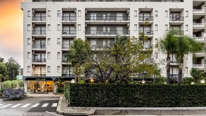 A multi-story hotel with balconies, a well-maintained hedge, and a clear pedestrian crossing.