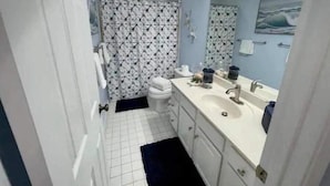 A bathroom with a white toilet, a sink with a mirror, and a patterned shower curtain. - Tybee Island Silver Ave Retreat (Tybee Island)