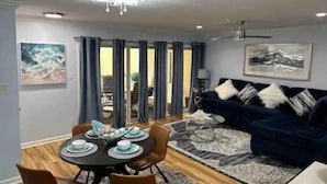 A modern living room with a dark blue sofa, a dining table set with plates and bowls, and a patterned rug. - Tybee Island Silver Ave Retreat (Tybee Island)