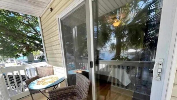 A covered outdoor area with a sliding glass door, a wicker chair, and a small table. - Tybee Island Silver Ave Retreat (Tybee Island)