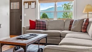 Una sala de estar con un sofá seccional, una mesa de centro de madera, una lámpara y una ventana con vistas al exterior.