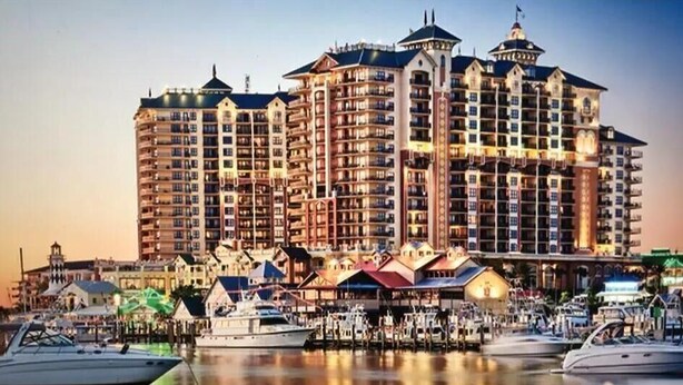 A large hotel with multiple floors and balconies, situated by a marina with boats docked.