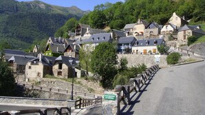 Un village perché sur une colline, avec des maisons en pierre, une route et un panneau indiquant « Chambres d’hôtes ».