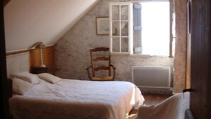 A bedroom with a sloped ceiling, a bed, a chair, a radiator, and a window with curtains. - Chalet de Caractère, balcon sur les Pyrénées, à 5 min de la station Saint Lary (Saint-Lary-Soulan)