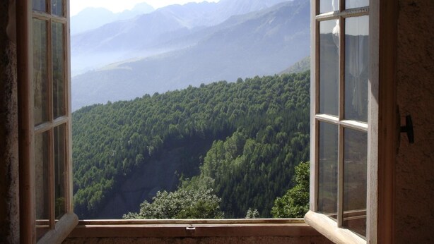 Une fenêtre donnant sur une vallée boisée et des montagnes lointaines.