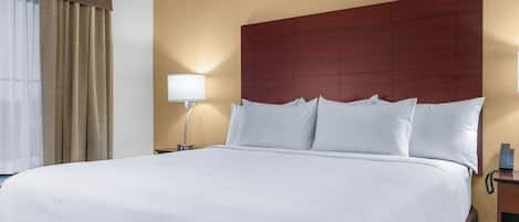 A large bed with white linens, a wooden headboard, a bedside lamp, and a telephone on a wooden nightstand.